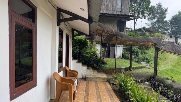 A covered porch with a wooden bench, a white wall, and a garden with plants and a wooden fence. - Masada Village (Cisarua)
