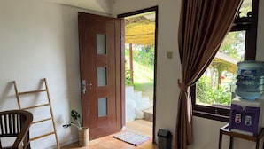 A room with a wooden door, a chair, a water dispenser, and a view of the outdoors. - Masada Village (Cisarua)