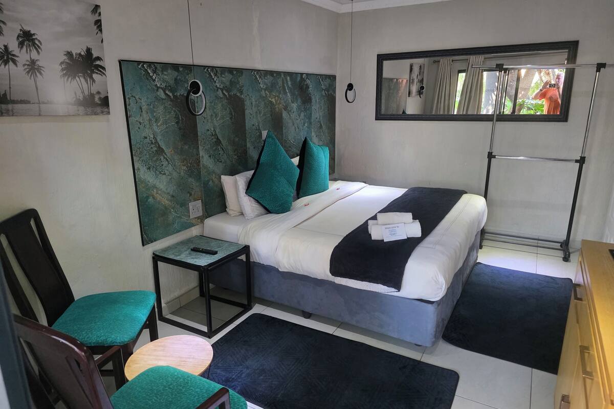 Un dormitorio con cama, mesita de noche, silla, espejo y ventana.