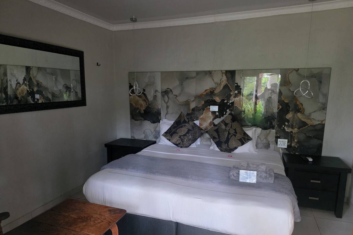 Un dormitorio con cama, dos mesitas de noche, un banco y una obra de arte colgada en la pared.