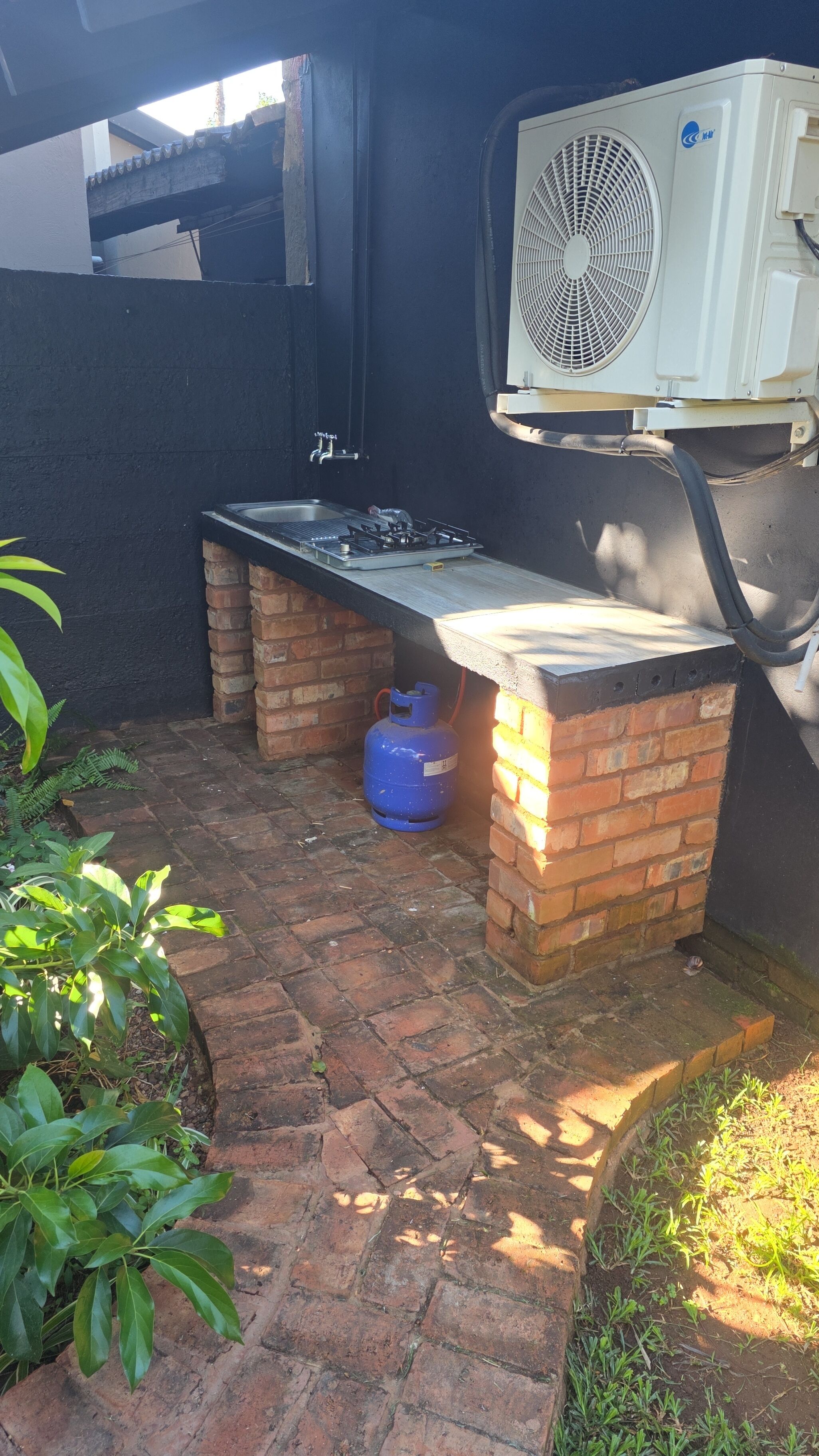 An outdoor kitchen area with a gas stove, a blue propane tank, and an air conditioning unit mounted on a wall.