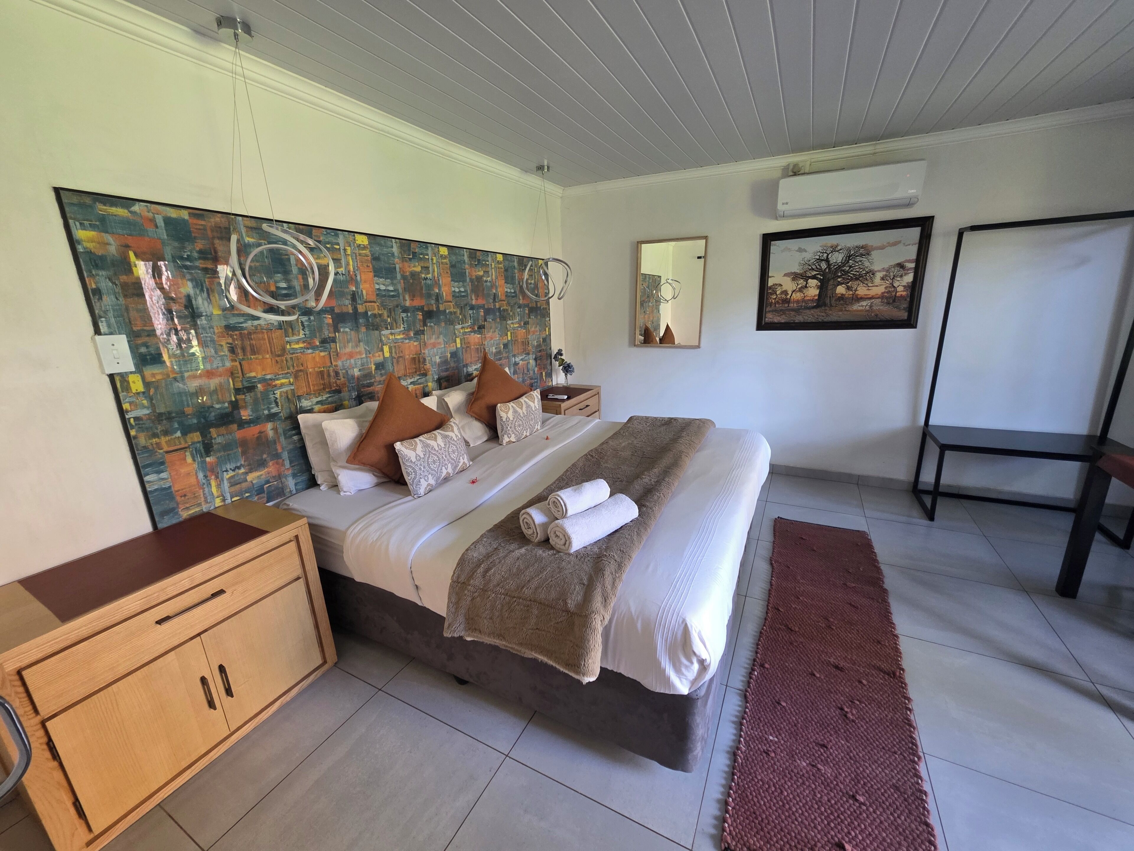 A bedroom with a large bed, a wooden cabinet, a mirror, and a painting on the wall.