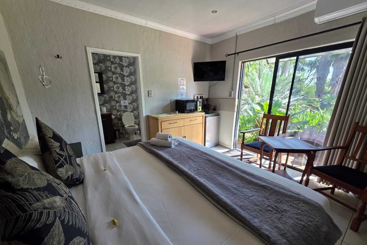 Habitación de hotel con cama, escritorio con computadora, televisión y balcón con sillas.
