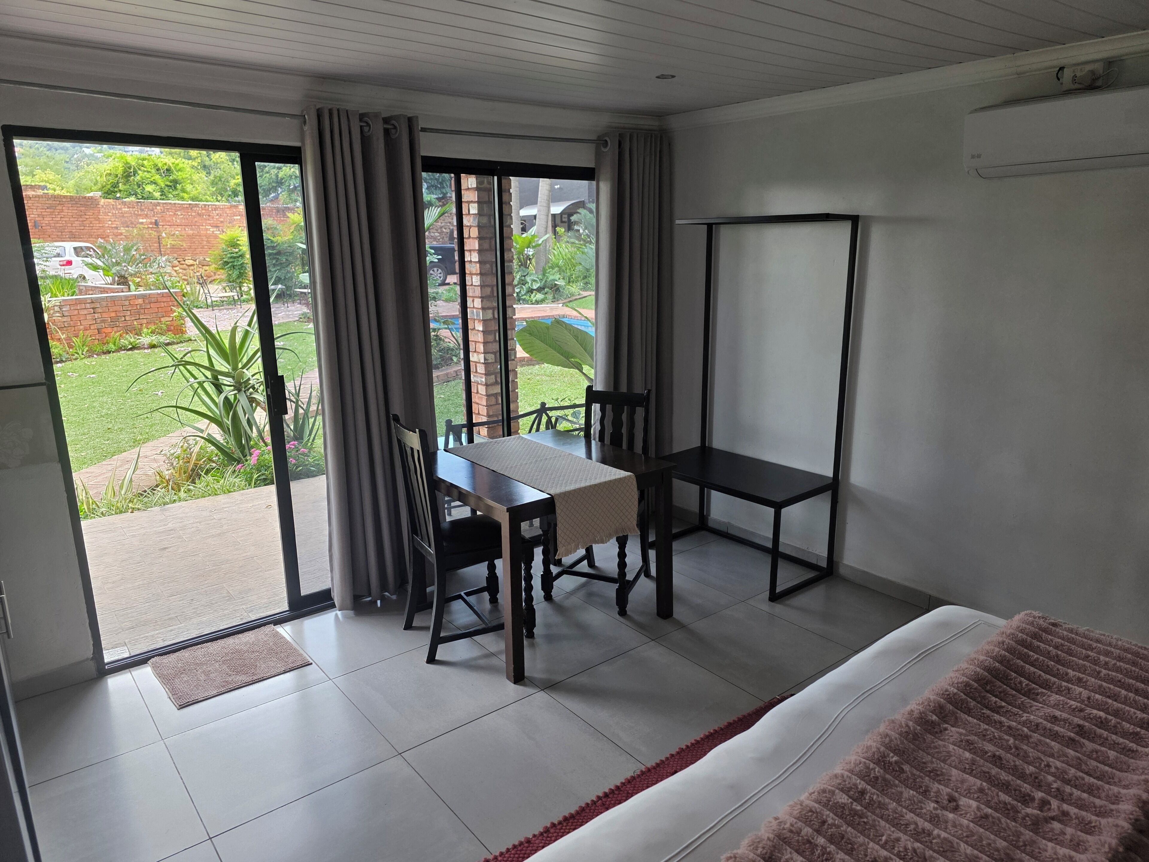Una habitación con cama, una mesa con sillas, un ventanal con cortinas y un equipo de aire acondicionado.