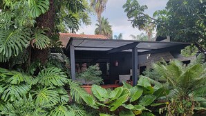 Un espacio de estar al aire libre cubierto, con una mesa y sillas, rodeado de exuberante vegetación tropical.