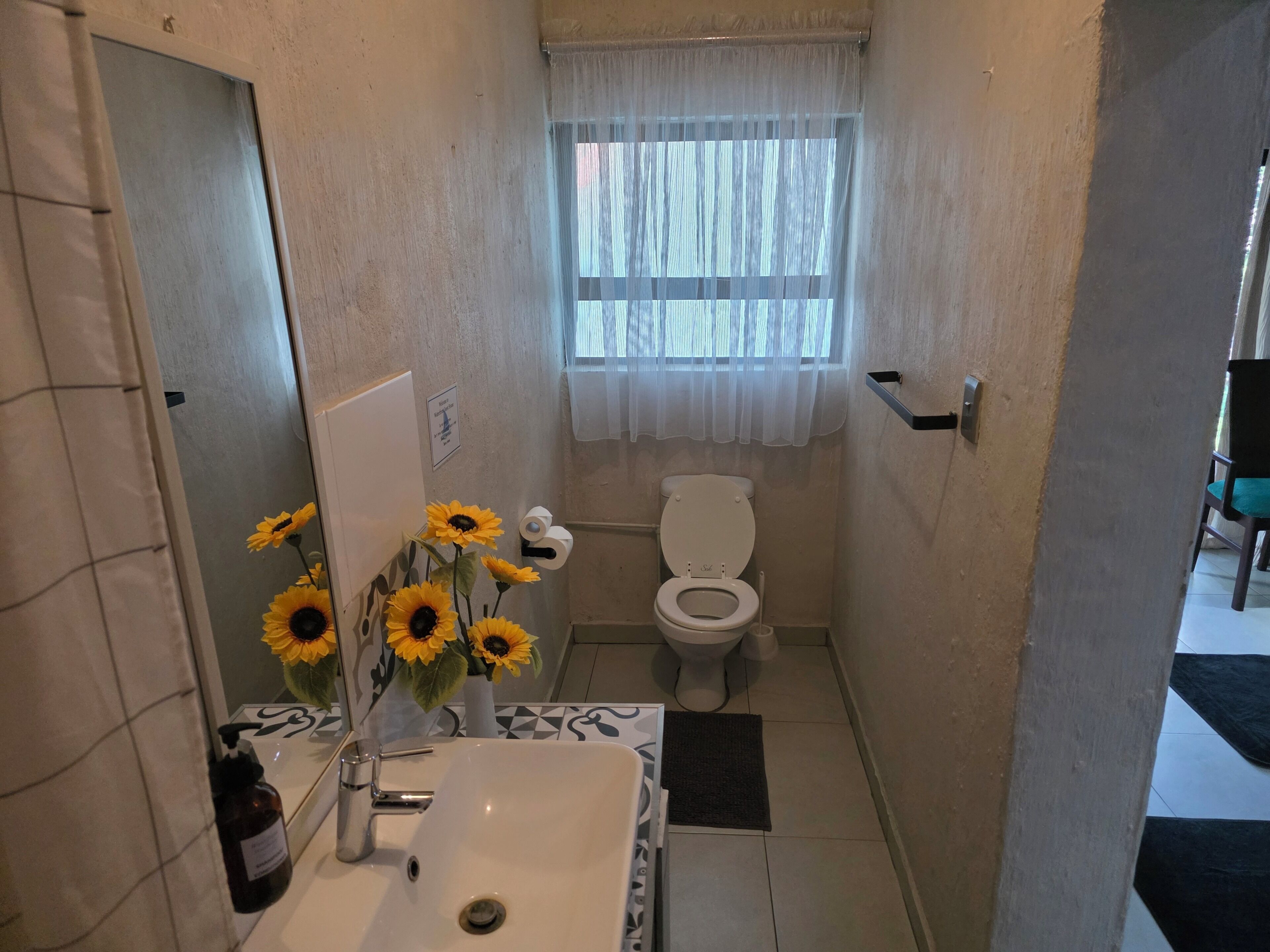 A bathroom with a sink, toilet, and a window with sheer curtains.