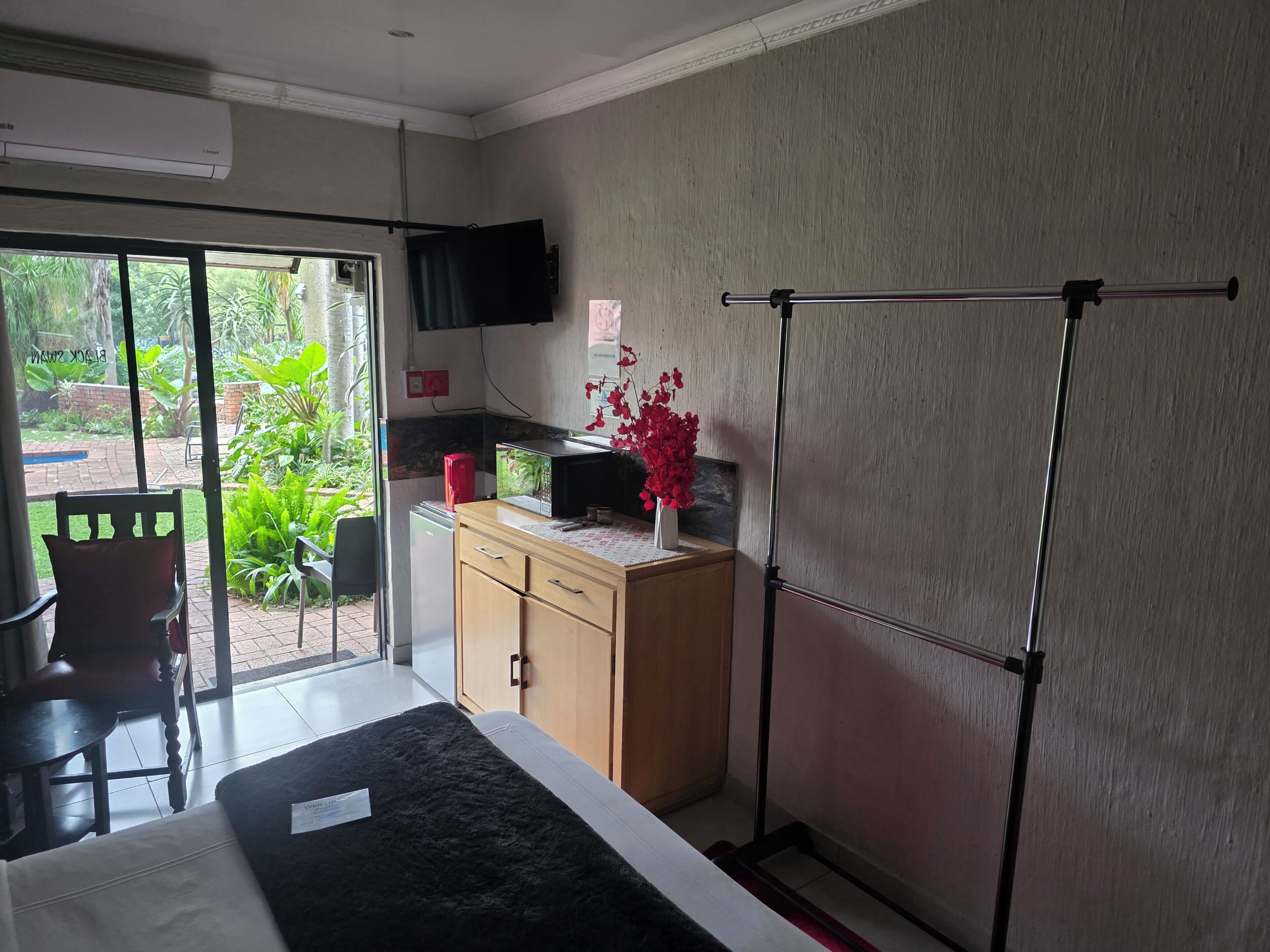 Habitación de hotel con cama, escritorio con computadora, televisor montado en la pared y vista al jardín exterior.