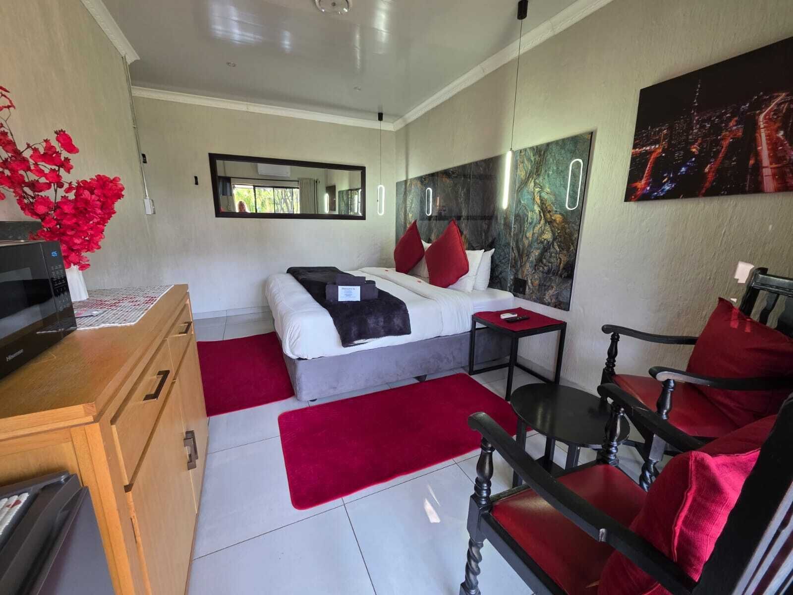 A hotel room with a bed, a desk, a chair, a microwave, and a red flower arrangement.