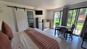 Un dormitorio con cama, escritorio, silla, televisor y puerta corrediza de vidrio que da a un balcón.