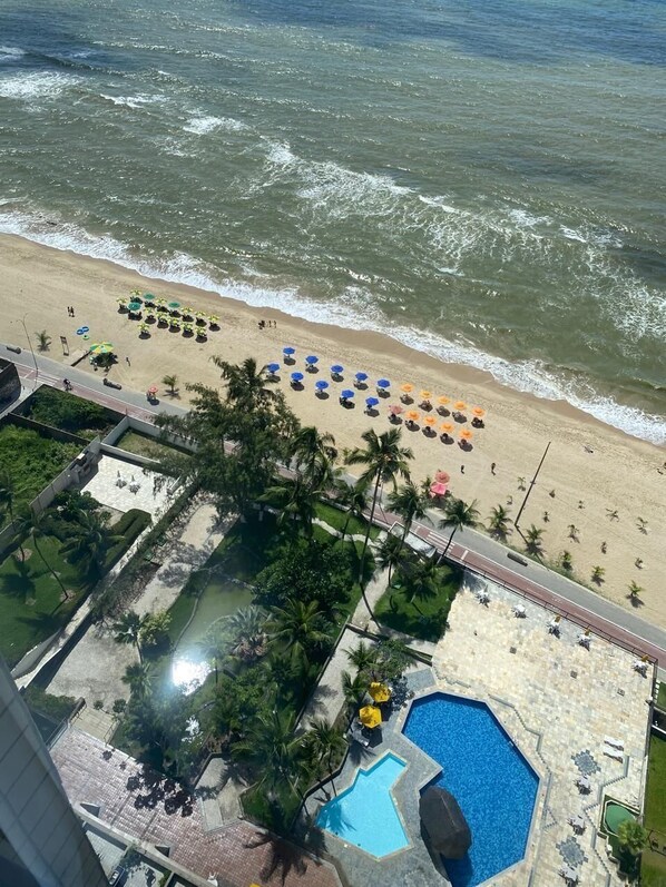 Un complejo turístico en la playa con piscina, sombrillas y palmeras.