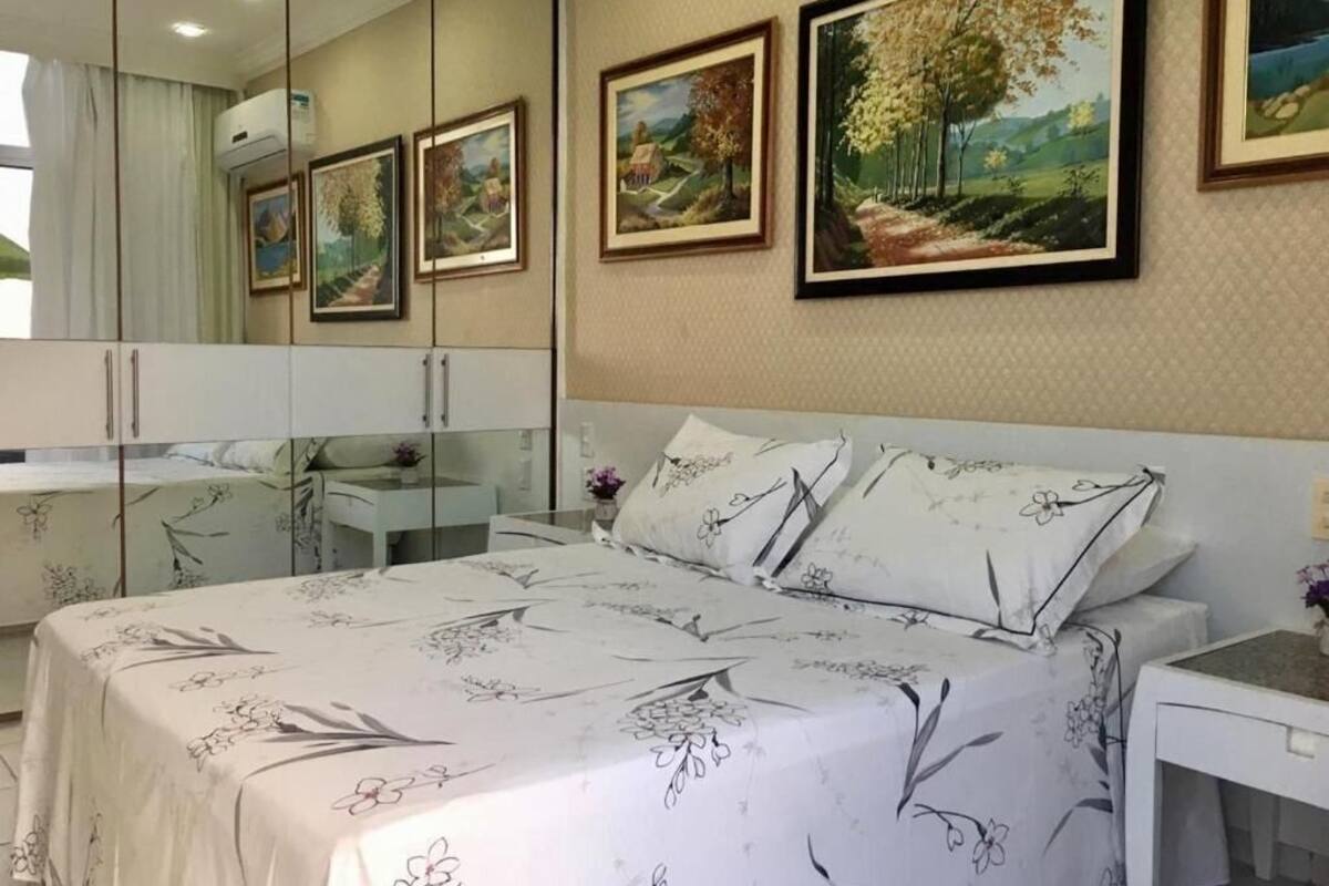 Un dormitorio con una cama grande, una mesita de noche, un espejo y pinturas de paisajes enmarcadas en la pared.