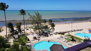 Vista de una playa con piscina, palmeras y sillas de playa.