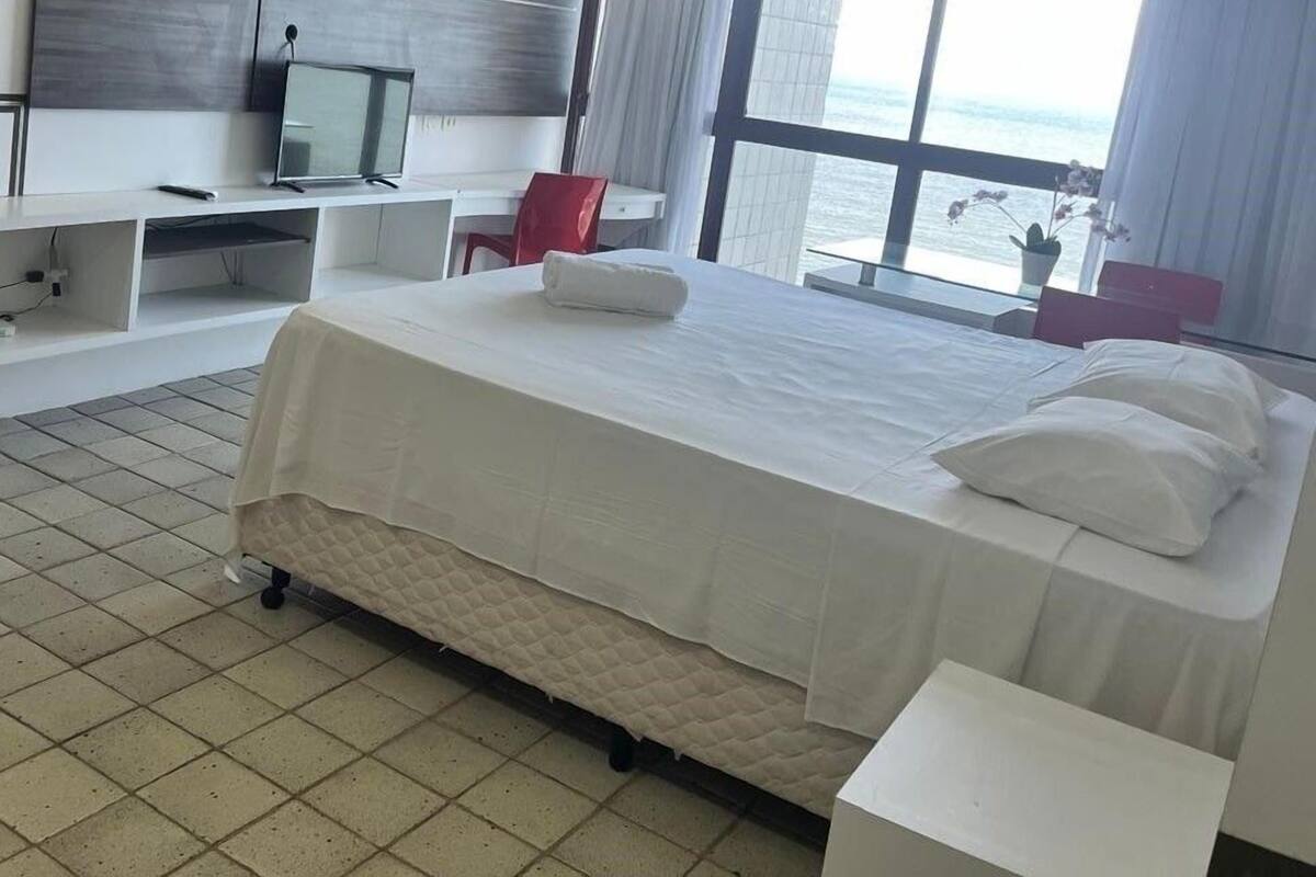 Una habitación de hotel con cama, escritorio, televisión y un ventanal grande.