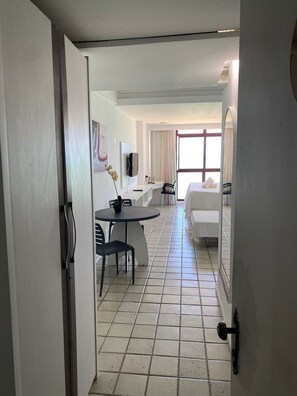 A hotel room with a bed, a desk, a chair, a small table, and a window with curtains. - FLATS GOLDEN BEACH APARTMENTS (Jaboatão dos Guararapes)