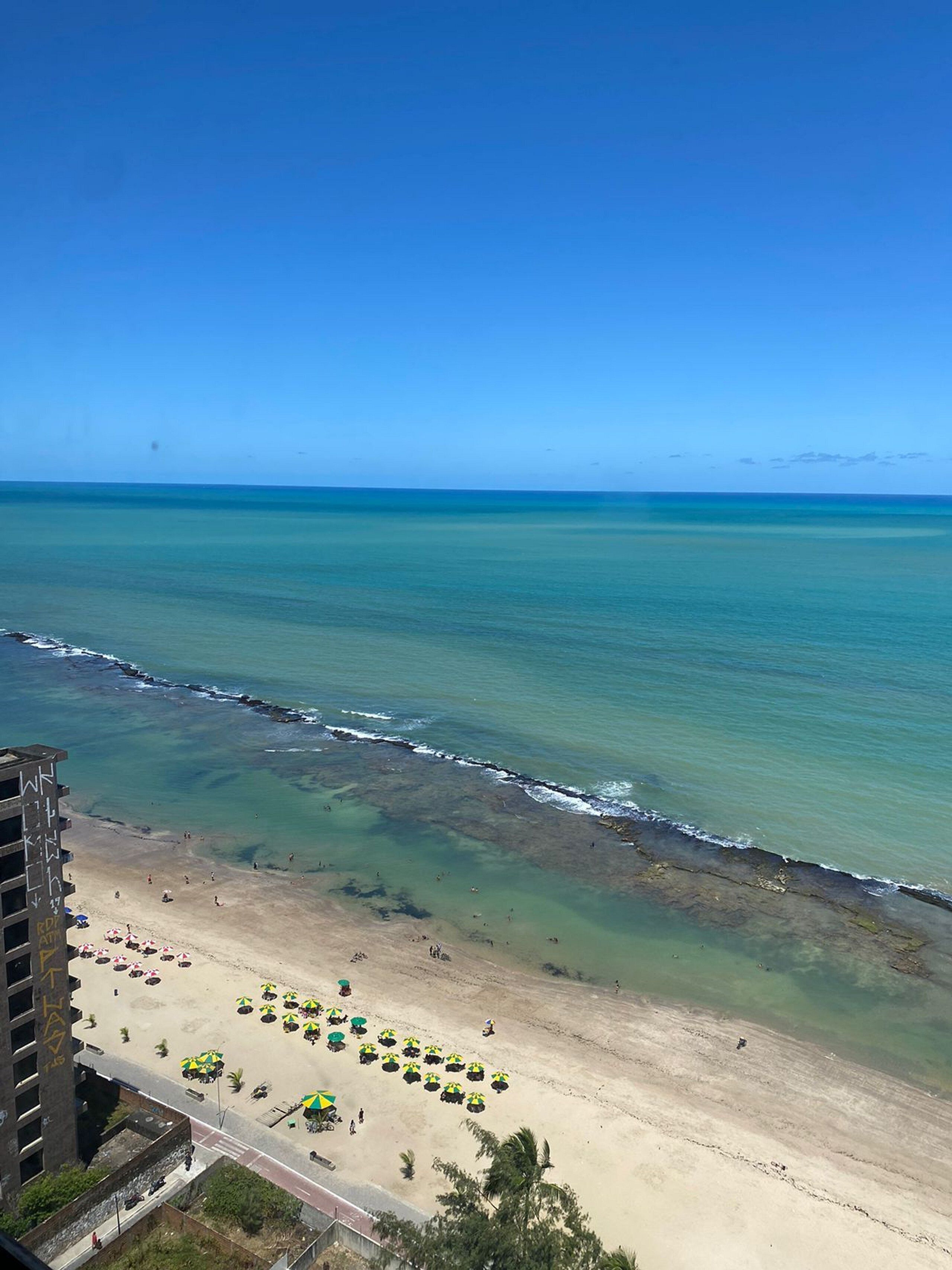 A beach view with clear skies, a sandy shore, and a building with graffiti.