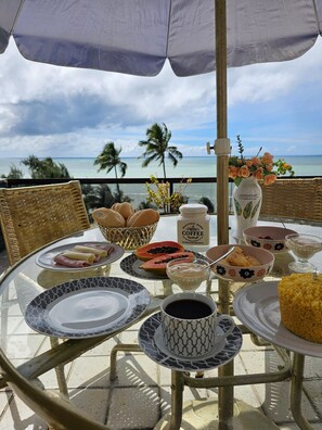 A table set for breakfast with a view of the ocean, including plates, bowls, and a coffee pot. - FLATS GOLDEN BEACH APARTMENTS (Jaboatão dos Guararapes)