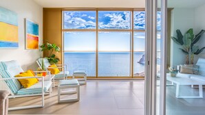 Ein modernes Zimmer mit großem Fenster und Meerblick, inklusive Balkon mit Sitzgelegenheit.