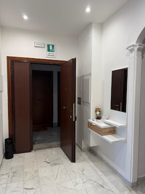 Une chambre d’hôtel avec un sol en marbre, une porte en bois, un comptoir d’accueil blanc et un miroir.