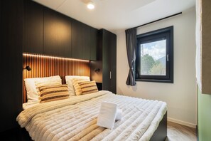 Ett modernt hotellrum med en stor säng, en mörk träfärgad sänggavel och ett fönster med gardiner.