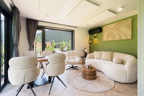Ein modernes Wohnzimmer mit einer Couch, Sesseln, einem runden Couchtisch und Blick auf eine Berglandschaft durch große Fenster.