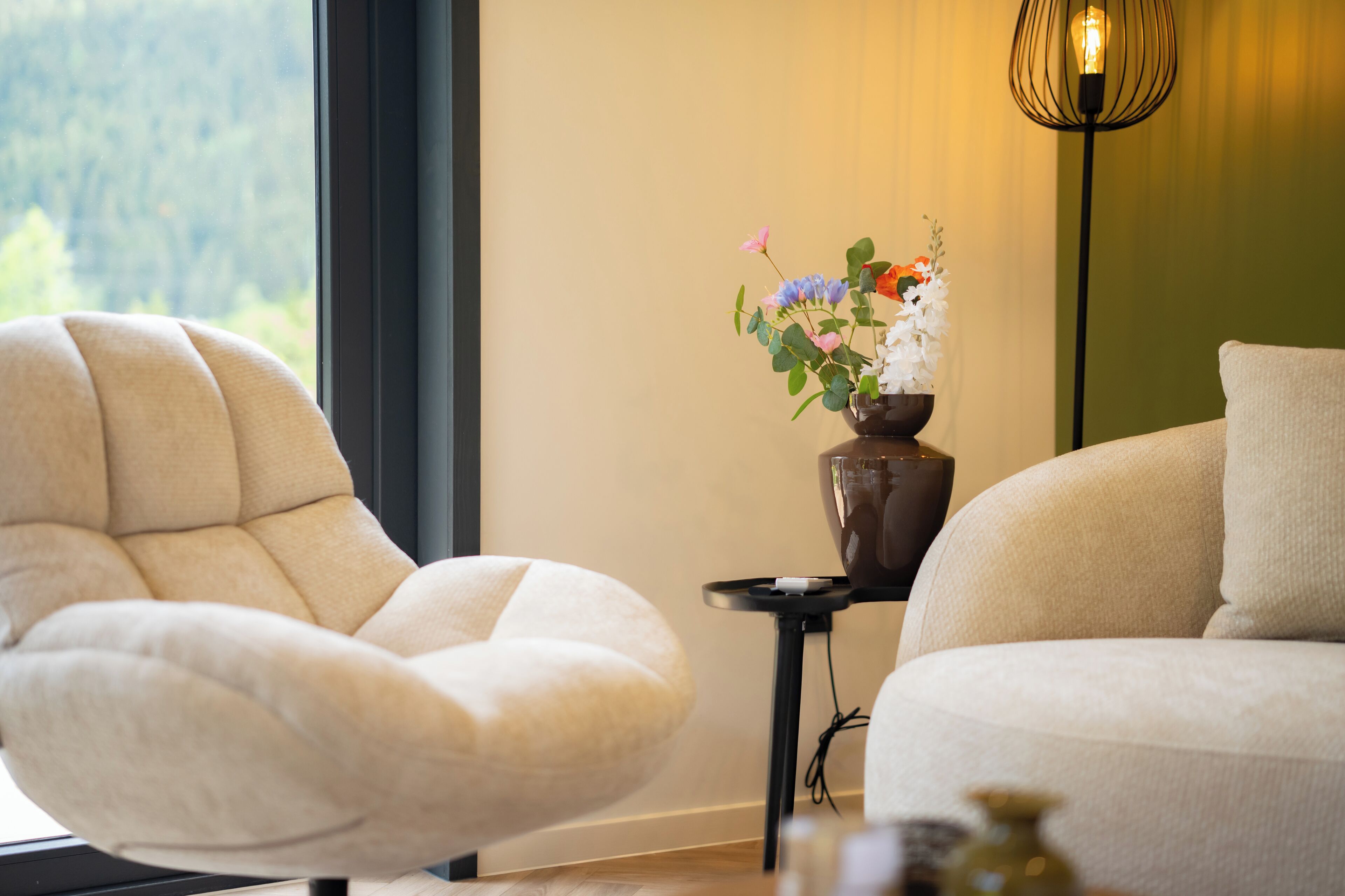 A modern living room with a sofa, a chair, a vase with flowers, and a floor lamp.