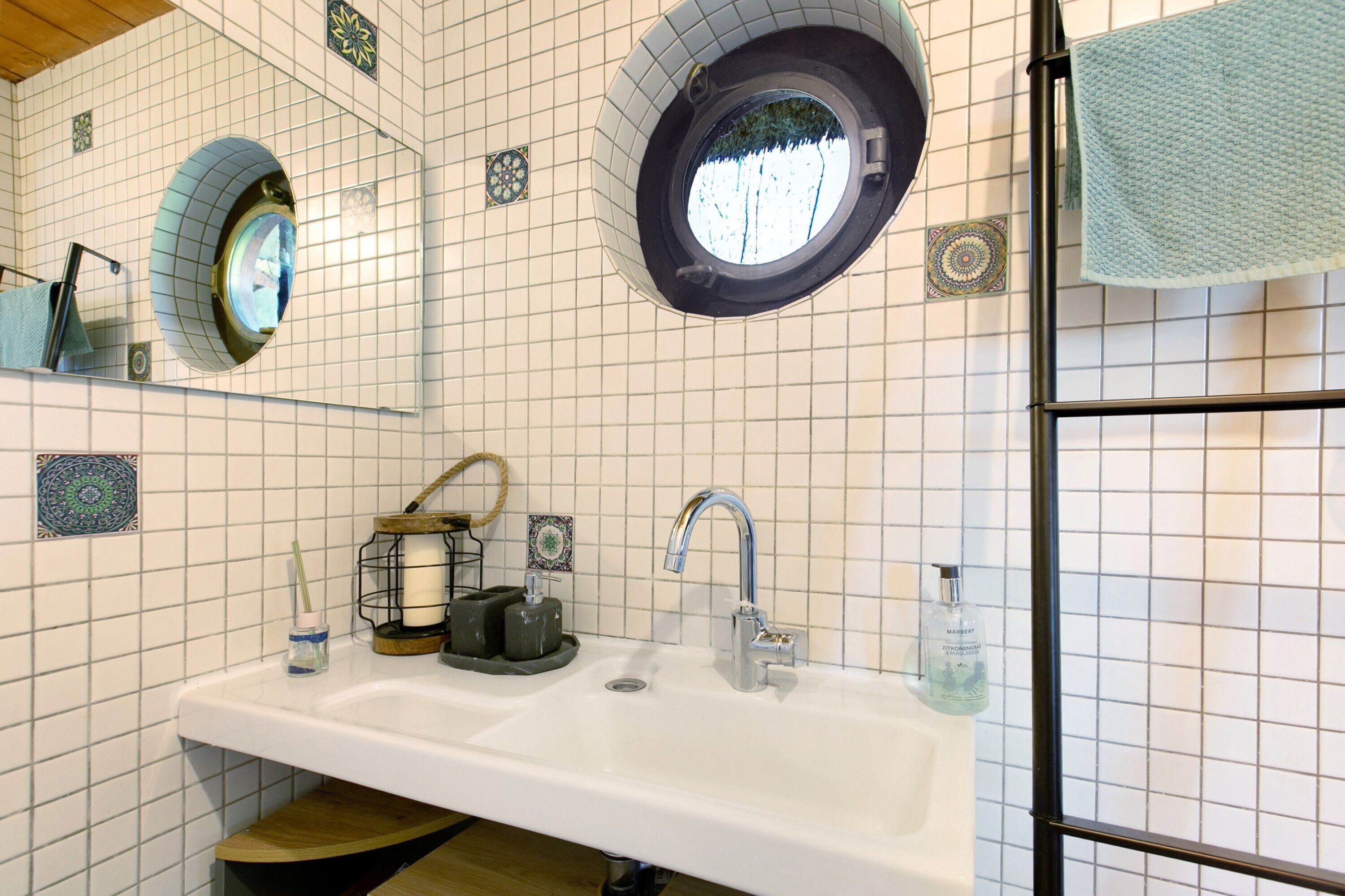 Een badkamer met een wastafel, twee spiegels, een handdoekhouder en een raam.