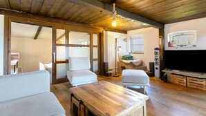 Una habitación acogedora con suelo de madera, un televisor de pantalla plana grande y un techo rústico.