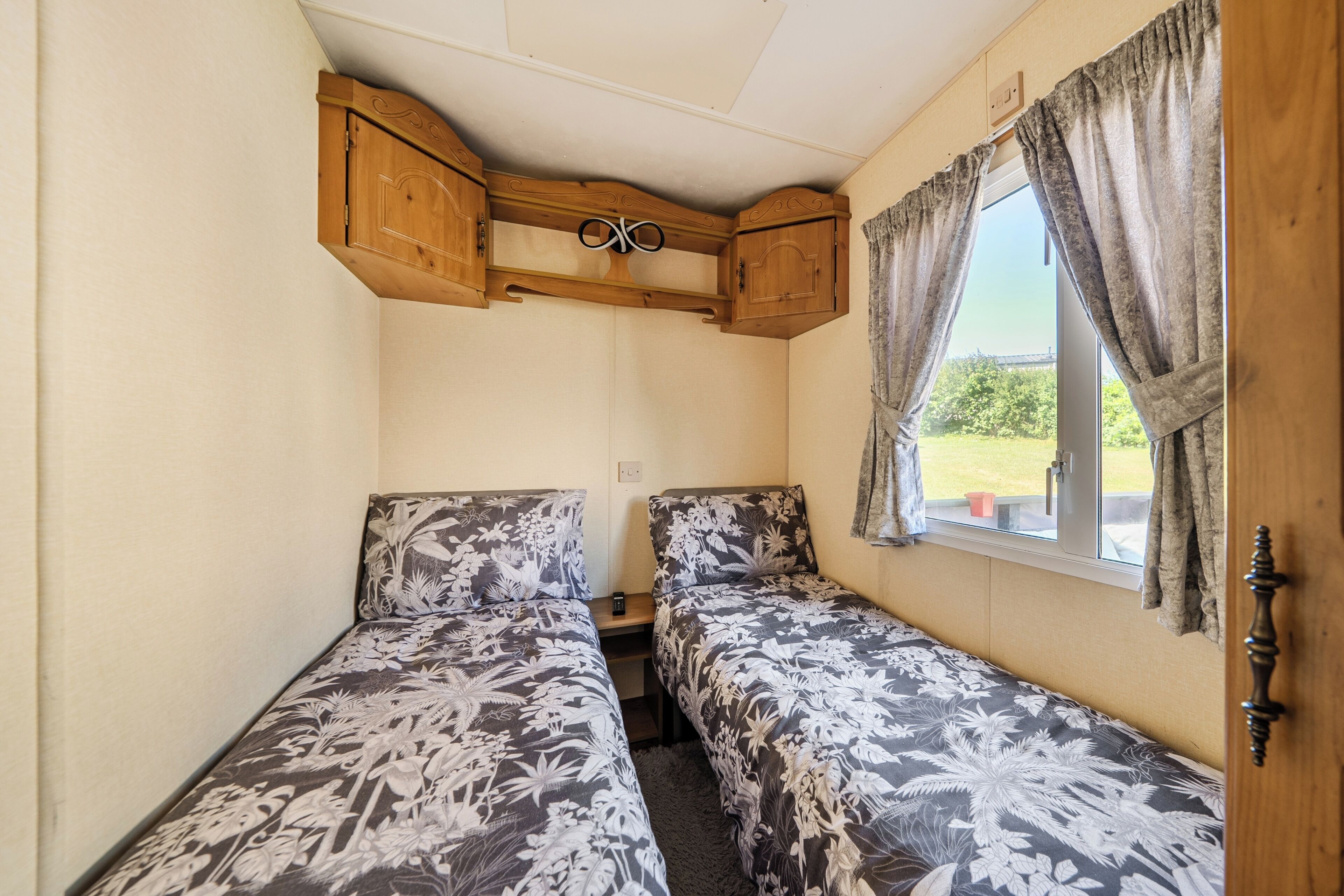 A small room with two beds, wooden cabinets, and a window with curtains.