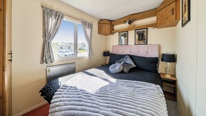 A bedroom with a bed, a window, a radiator, a bedside table, and a lamp. - 3 Bed - Sleeps 8 - Sea View - Pets - Parking (Filey)
