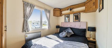 Un dormitorio con cama, ventana, radiador, mesita de noche y lámpara.
