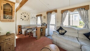 A cozy room with a wooden ceiling, a large wall clock, a sofa, a dining table, and a wooden cabinet. - 3 Bed - Sleeps 8 - Sea View - Pets - Parking (Filey)