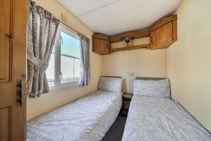 Une chambre compacte dans un camping-car, comprenant deux lits, une fenêtre avec des rideaux et des meubles en bois.