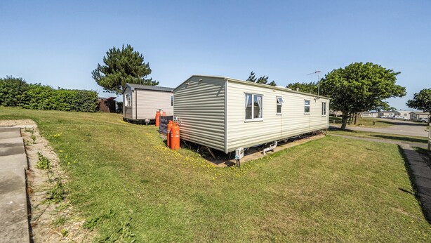 A mobile home with a small attached garage, a lawn, and a clear sky. - 3 Bed - Sleeps 8 - Sea View - Pets - Parking (Filey)