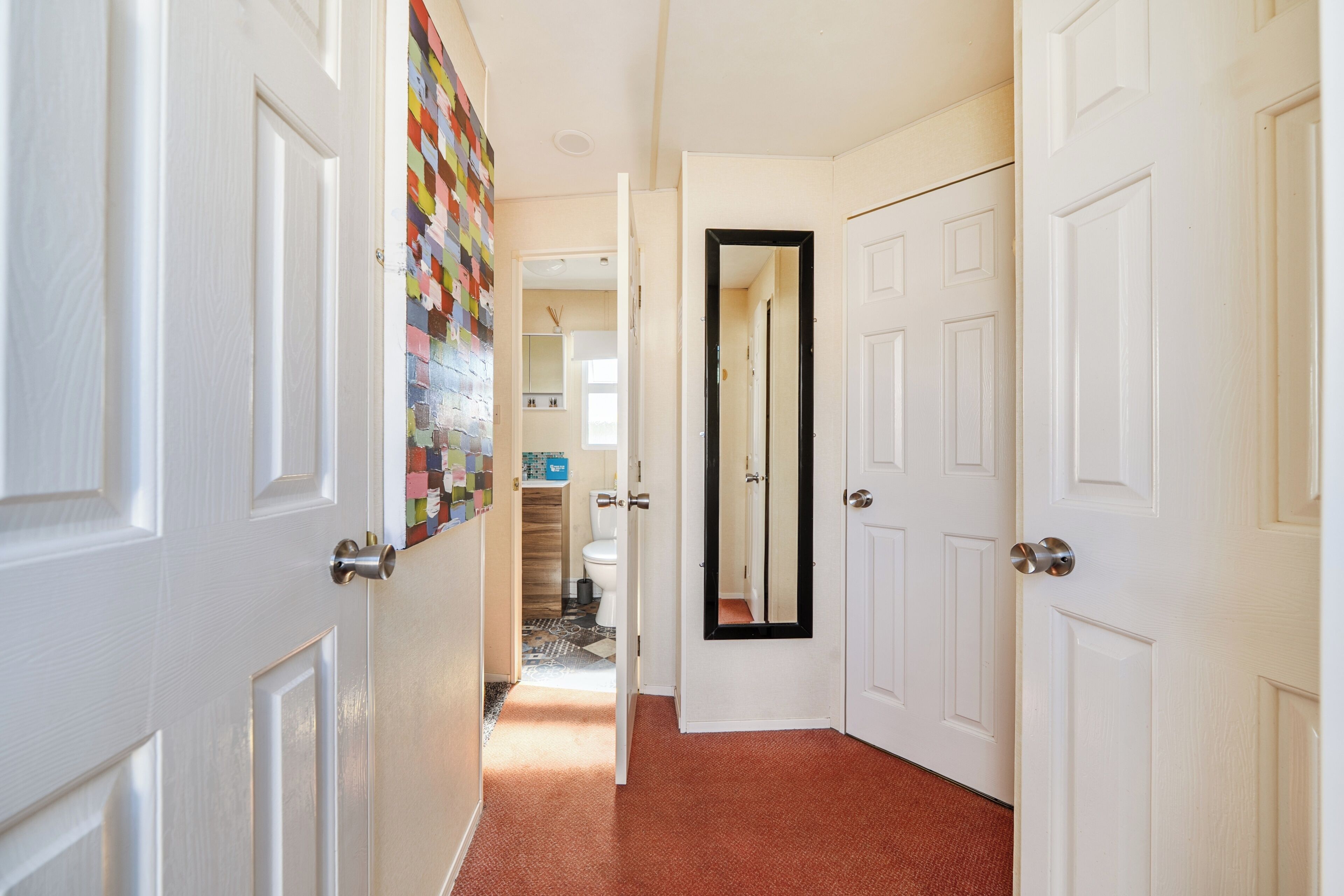 A hallway with white doors, a colorful wall, and a mirror on one door.