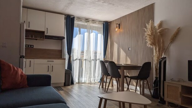 Un salon moderne comprenant un canapé, une table à manger avec des chaises, un coin cuisine avec des placards et une grande fenêtre avec des rideaux.