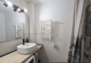 Een badkamer met een witte wastafel, een spiegel, een handdoekrek en een douchegordijn met bladmotief.