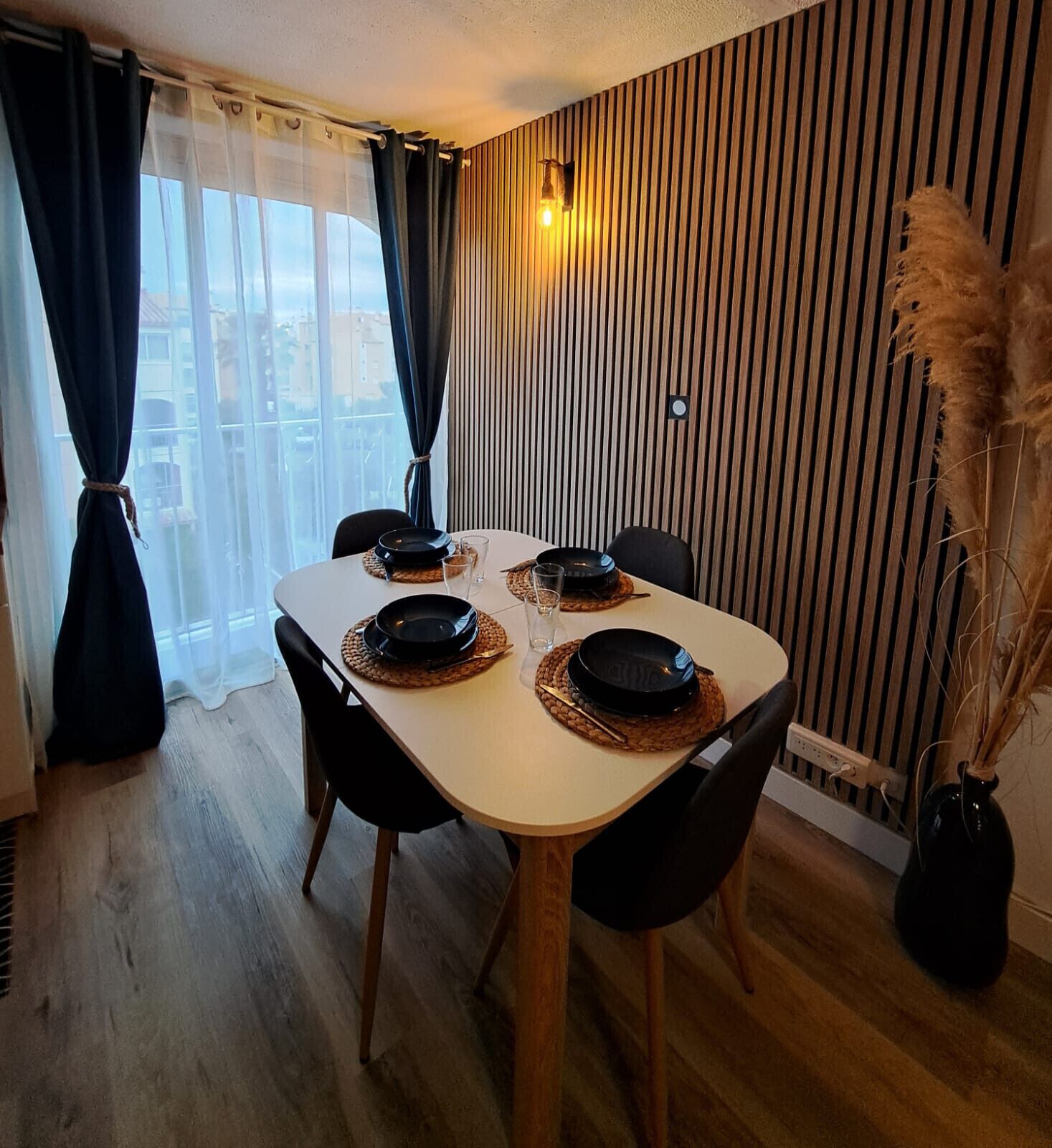 Ein Essbereich mit Tisch für vier Personen, Holzwandverkleidung und Blick durch das Fenster.