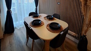 Un coin repas avec une table dressée pour quatre personnes, un lambris en bois sur le mur et une vue par la fenêtre.