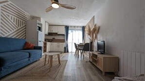 Un salon moderne avec un canapé bleu, une petite table, un téléviseur et un ventilateur de plafond.