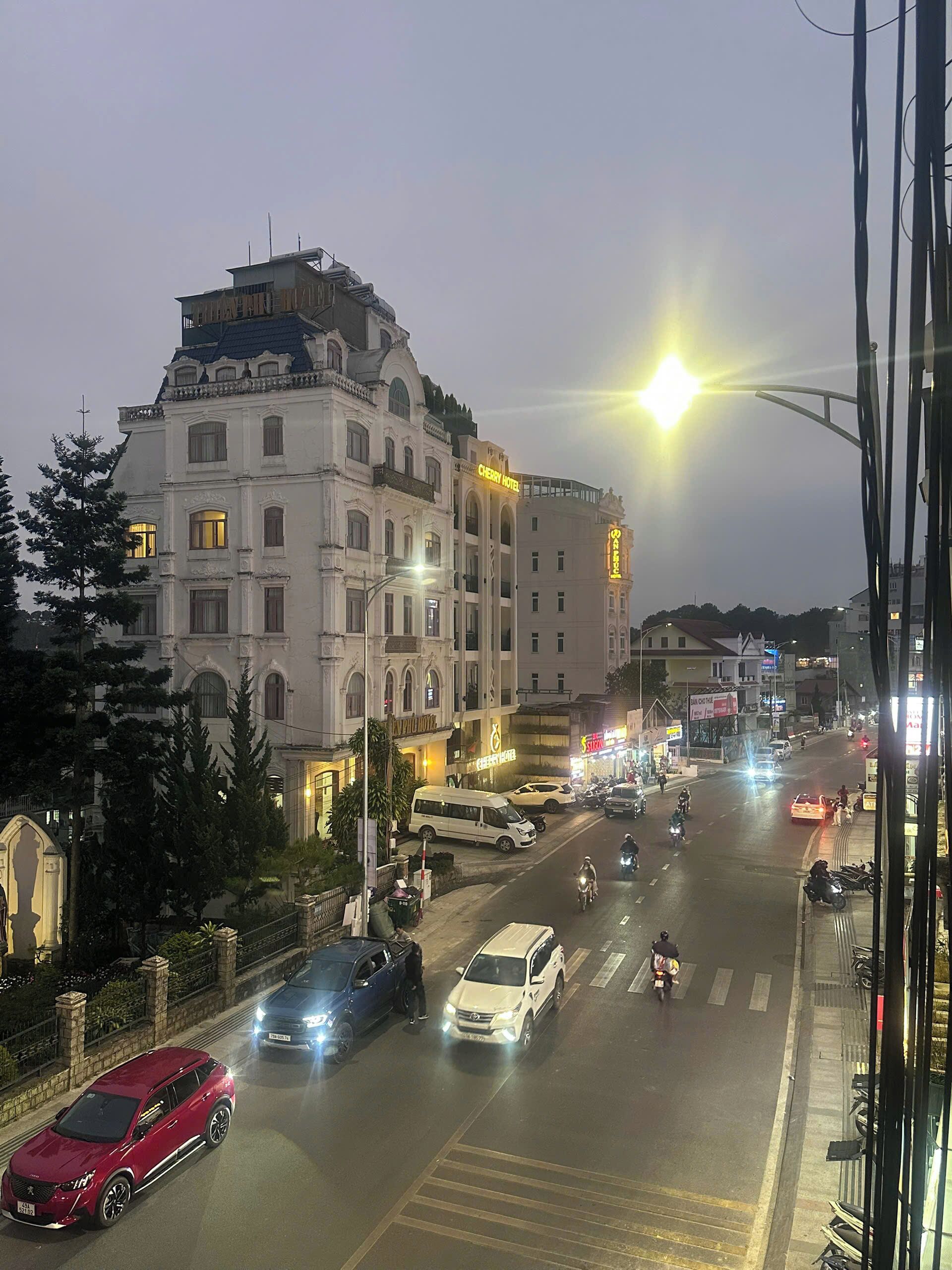 Un edificio de varios pisos con un llamativo letrero que dice 'Cherry Hotel', una calle con vehículos y un paso de peatones.