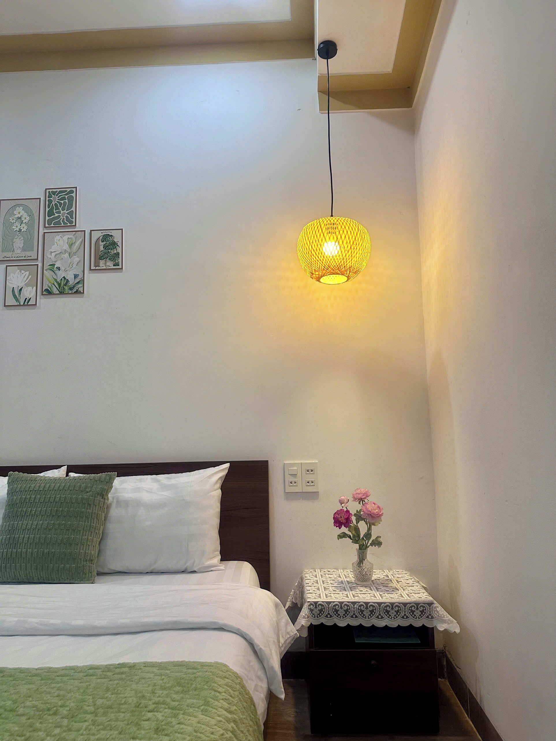 A bedroom with a bed, pillows, a bedside table with a vase of flowers, and wall art.