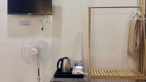 A room with a TV, a fan, a kettle, a refrigerator, a shelf with slippers, and a hanging rack with towels. - Van Nhi MTV Hotel (Xuan Huong - Da Lat)
