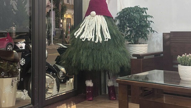 A gnome decoration near a window with a Christmas wreath, a potted plant, and a wooden table. - Van Nhi MTV Hotel (Xuan Huong - Da Lat)