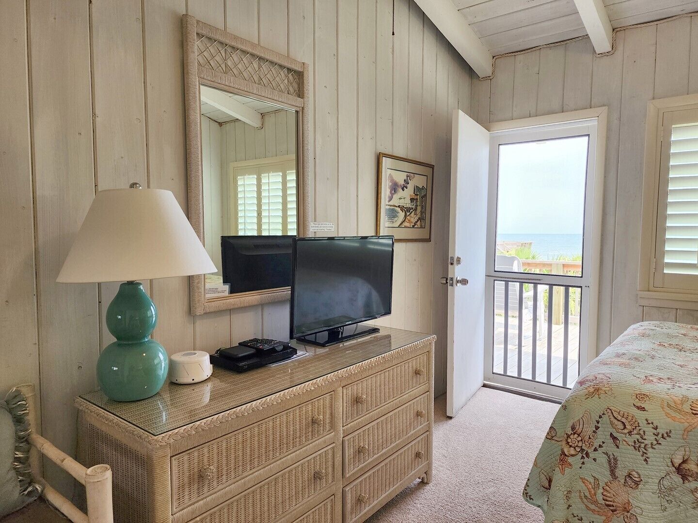 A room with a television on a dresser, a lamp, a framed picture, and a door leading to a balcony with a view.
