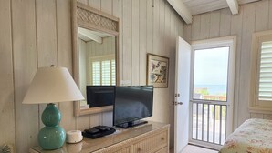Ein Zimmer mit Fernseher auf einer Kommode, einer Lampe, einem gerahmten Bild und einer Tür, die auf einen Balkon mit Blick führt.