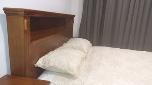 Een houten bed met hoofdbord, twee kussens en een nachtkastje van hout.