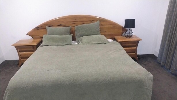Een bed met een houten hoofdeinde, twee nachtkastjes en een lamp op één nachtkastje.