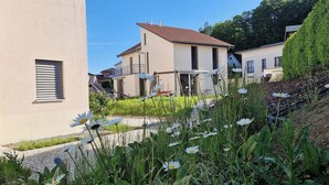 Zona residencial con casas, un sendero pavimentado y un jardín con flores blancas.