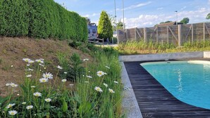 Una piscina con cubierta de madera, setos verdes y valla.