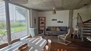 Ein modernes Wohnzimmer mit Essbereich, einer Treppe und Blick durch große Fenster.
